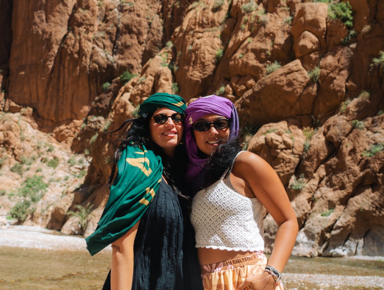Two female group travellers pose with the epic backdrop of Todra Gorge in Morocco